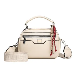 Elegante beige Handtasche aus Kunstleder mit gemustertem Gurt und roten Quasten