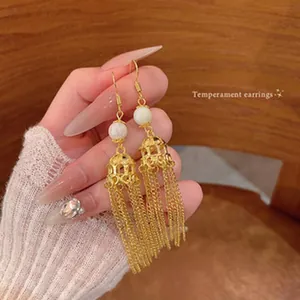 Macro detail of handmade gold tassel earrings with white pearl bead and woven cage design