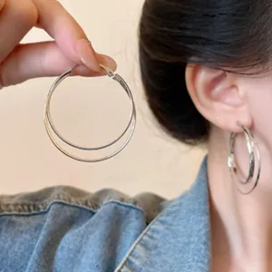 Detailed close-up of silver double hoop earrings worn on ear and held in hand for scale