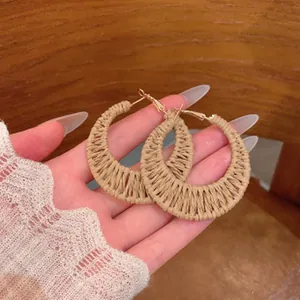 Close-up of handmade straw woven moon earrings held in hand for vacation style.
