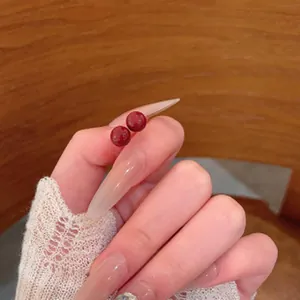 Detailed view of small retro red round bead earrings held by hand with long nails