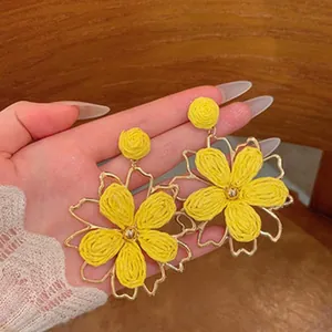 Close-up detail of handmade yellow straw woven flower earrings featuring a gold metal frame