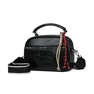 Elegante kleine Handtasche aus schwarzem Leder mit breitem Schultergurt und Anhängern