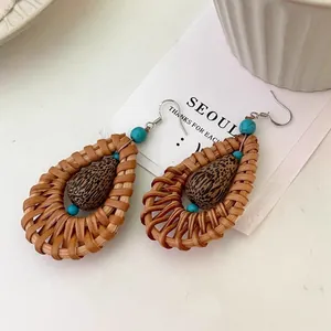 Close-up of handmade rattan teardrop earrings with turquoise beads in boho style.