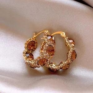 Macro detail of French style gold petal-shaped hoop earrings with brown crystals on silk