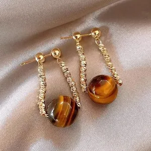 Dettaglio di orecchini vintage a perno con perle occhio di tigre e barre dorate lucide.