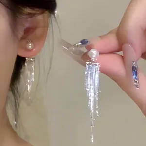Macro detail of elegant pearl earrings featuring long silver fringe tassels on ear