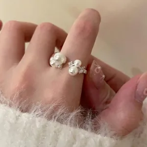 Nahaufnahme eines eleganten offenen Rings mit weißen Perlen und Zirkonia am Finger