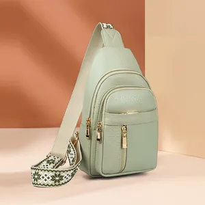 Detail of mint green leather chest bag featuring ethnic pattern strap and gold zippers.