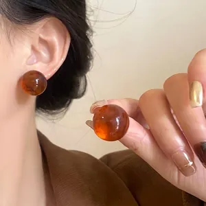 Amber brown resin ball stud earrings shown on model ear for aesthetic fashion look