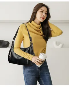 Detalle de un elegante bolso de hombro negro con múltiples cremalleras sostenido por una modelo