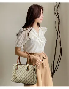Elegant monogram handbag with top handles held by a woman in a chic stylish outfit.