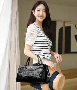 Elegant black crocodile embossed handbag held by a model in a bright stylish interior.