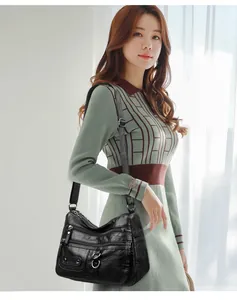 Elegant Asian model showcasing a black multi-pocket soft leather shoulder bag by a window
