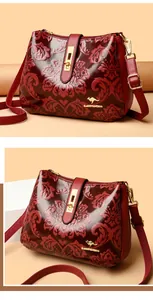Macro detail of burgundy embossed floral crossbody bag with gold-tone hardware