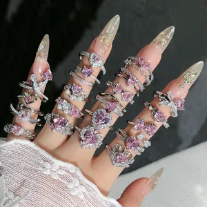Primer plano de varios anillos de corazón rosa brillantes en dedos con uñas decoradas