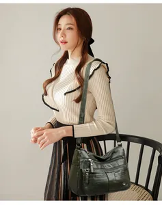 Lifestyle view of a dark green multi-pocket crossbody bag worn by a stylish model