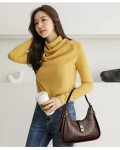 Detail view of a dark brown embossed leather underarm bag styled with a yellow turtleneck