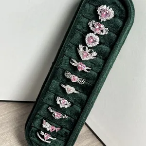 Vista detallada de varios elegantes anillos con forma de corazón rosa en una caja verde.