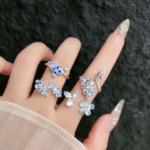 Vista detallada de anillos plateados con flores en esmalte azul degradado y pavo
