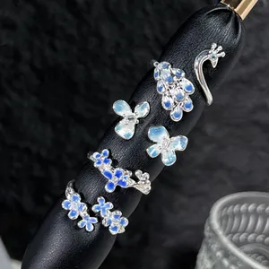 Primer plano detallado de anillos abiertos ajustables de esmalte degradado azul pavo y flores.