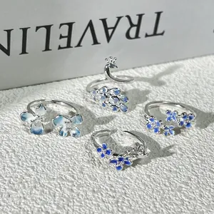 Vista detallada de cuatro anillos abiertos de plata con pavo real y flores azules.