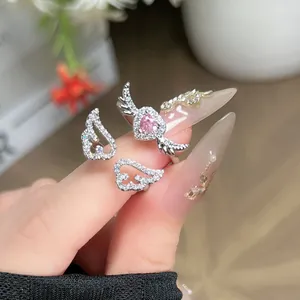 Detailed macro shot of sparkling angel wing rings with a pink heart stone on a finger.