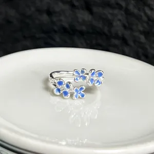 Primer plano de un anillo abierto de plata con flores de esmalte azul degradado y cristales.