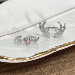 Close-up of silver-plated antler and heart wing rings with pink crystal on ceramic dish.