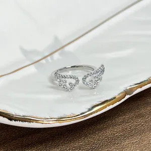 Detail of a minimalist silver-colored ring featuring elegant stone-encrusted wing motifs