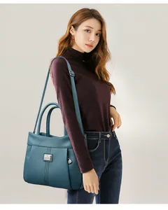 Model showcasing a teal pebbled leather handbag with adjustable shoulder strap