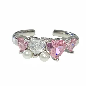 Primer plano de un anillo de corazón plateado con gemas rosas y detalles de perlas