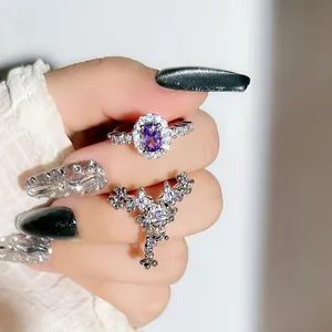 Close-up detail of silver floral tassel ring and oval purple stone ring on hand.