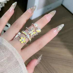 Primer plano de anillos de esmalte amarillo con mariposa, flor y perla