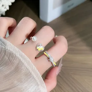 Primer plano macro de anillos plateados ajustables con mariposa amarilla y perlas