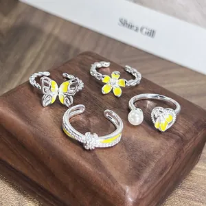 Vista detallada de anillos plateados con detalles de esmalte amarillo de mariposa y flor.