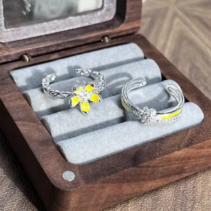 Detalle macro de anillos ajustables con flor amarilla y mariposa en caja de madera