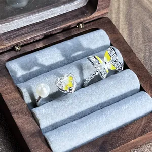 Detalle exquisito de anillos abiertos de plata con mariposa amarilla y perla en madera
