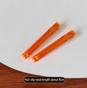 Detailed view of two minimalist transparent orange duckbill clips, 8cm long