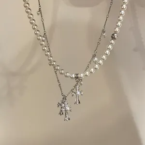 Close-up of double-layered necklace featuring white pearls and ornate cross pendants