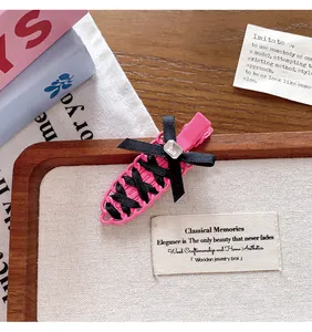 Detail of a balletcore style pink hair clip with black ribbon weaving and a small gem