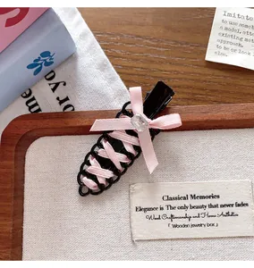 Close-up of ballet-style hair clip with pink ribbon weaving and crystal bow detail.