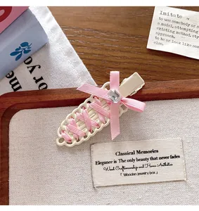 Detail view of a ballet-style woven pink ribbon hair clip with a sparkling gemstone bow.