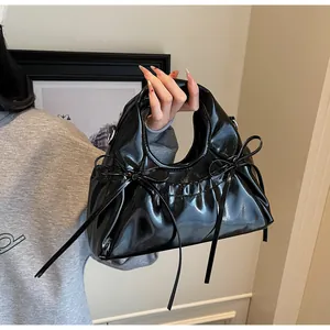 Bolso de mano elegante en charol negro con lazos decorativos y acabado brillante