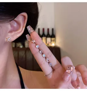Close-up of delicate multi-shape zircon stud earrings set on a model's hand and ear.