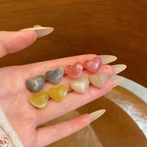 Detailed view of colorful semi-translucent heart-shaped stud earrings held in hand.