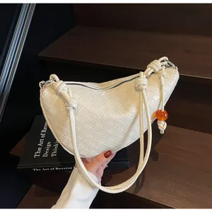 Primer plano de un bolso dumpling trenzado blanco con una cuenta de ámbar.