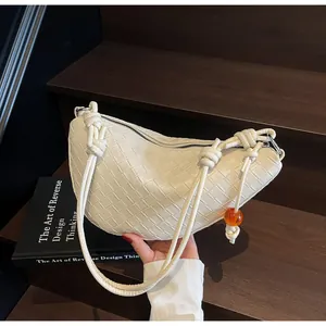 Primer plano de un bolso bandolera de cuero trenzado blanco sostenido sobre fondo de madera