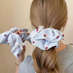 Dettaglio di uno scrunchie a quadretti azzurri con fragole e bordo in pizzo elegante.