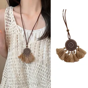 Retro ethnic long necklace with circular metal pendant and beige tassels on a model
